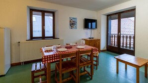 Uma sala de jantar com uma mesa posta para quatro pessoas, uma televisão na parede e uma janela com vista para um edifício.