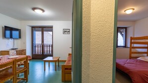 Quarto com uma mesa de madeira e cadeiras, uma cama, uma televisão e uma janela.