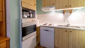 Cozinha compacta com armários de madeira, forno embutido, micro-ondas, lava-louças e pia com torneira moderna.