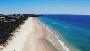 Luchtbeeld van een strand met heldere lucht, een zandstrand en enkele mensen die erover lopen.