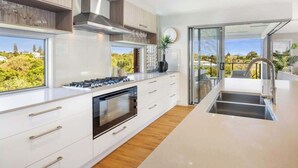 Een moderne keuken met witte kasten, een ingebouwde oven en een groot raam met uitzicht op groen.