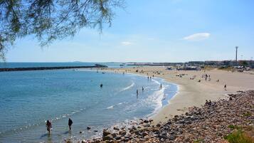 Une plage au rivage rocheux, avec une eau d’un bleu limpide, et quelques personnes visibles au loin.