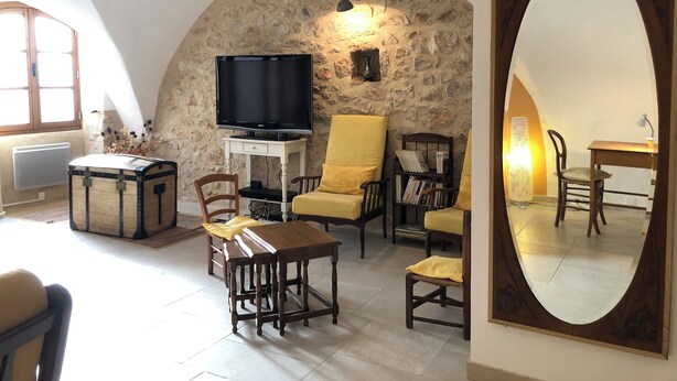 Una sala de estar acogedora con pared de piedra, televisor, mesa de madera y sillas amarillas.
