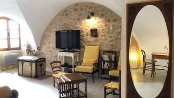 Un salon chaleureux avec un mur en pierre, un téléviseur, une table en bois et des chaises jaunes.
