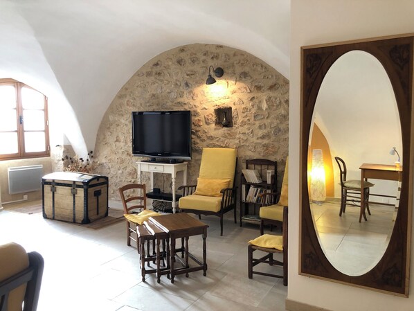 Una sala de estar acogedora con pared de piedra, televisor, mesa de madera y sillas amarillas.