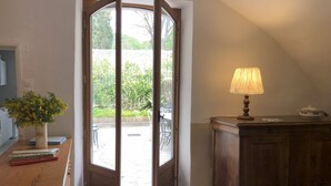 Una habitación con un escritorio de madera, una lámpara y vistas a un espacio exterior con plantas y una bicicleta.