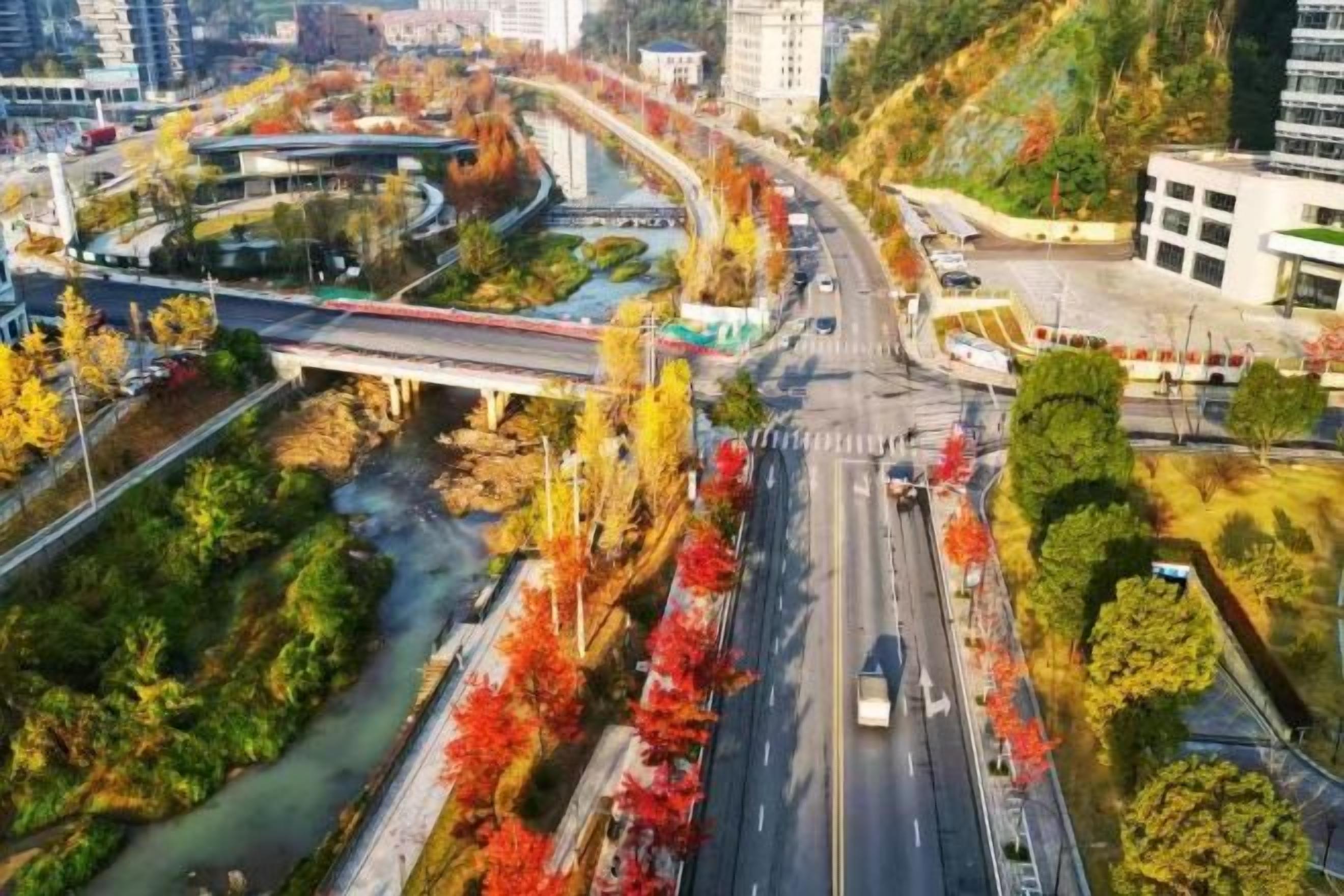 An aerial view of a cityscape with a river, a bridge, and a road with vehicles.