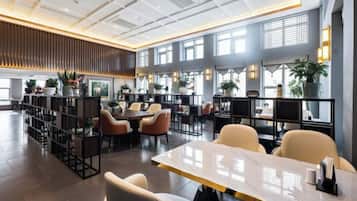 A spacious indoor area with multiple seating arrangements, including tables and chairs, and a variety of potted plants.
