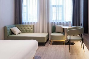 A hotel room with a green sofa, a small round table, and a white chair. - Kan Hotel (Suichang)