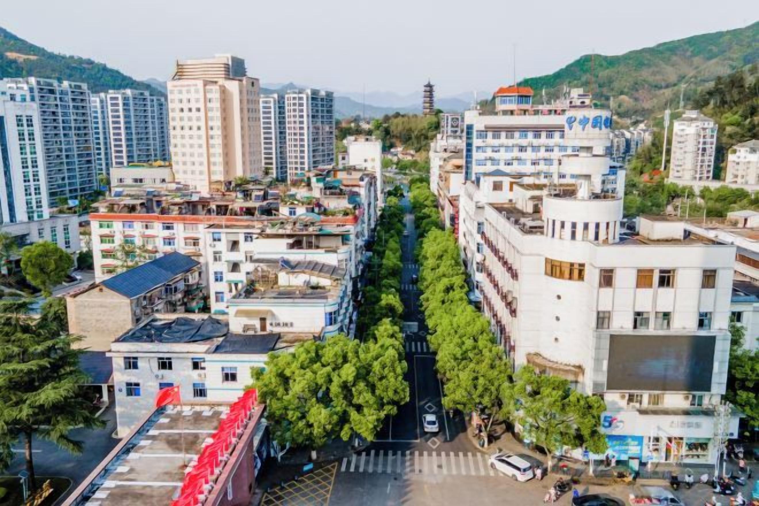 A cityscape with multi-story buildings, a tree-lined street, and a clear sky.