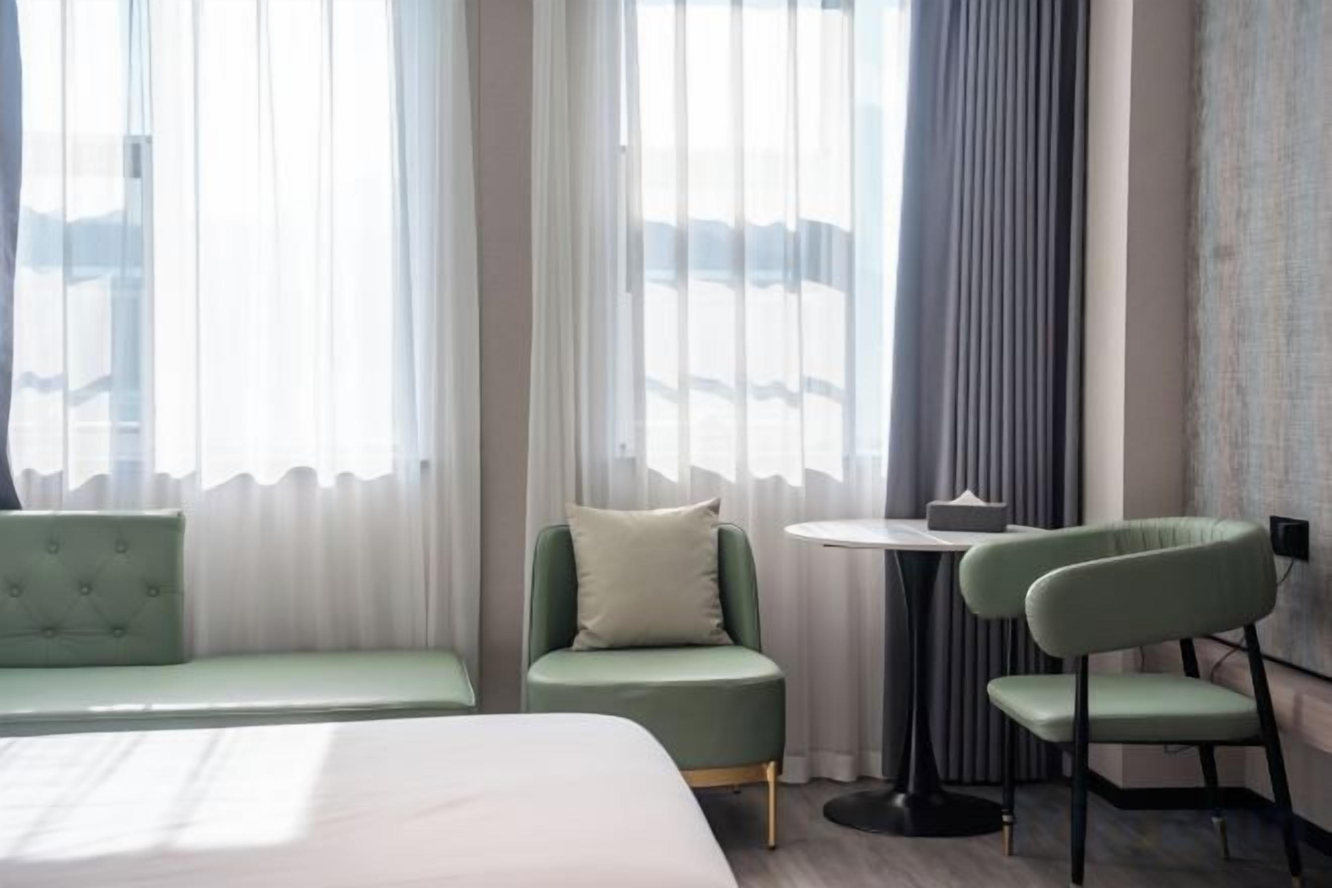 Et hotelværelse med en seng, en grøn sofa, et lille rundt bord og en stol.