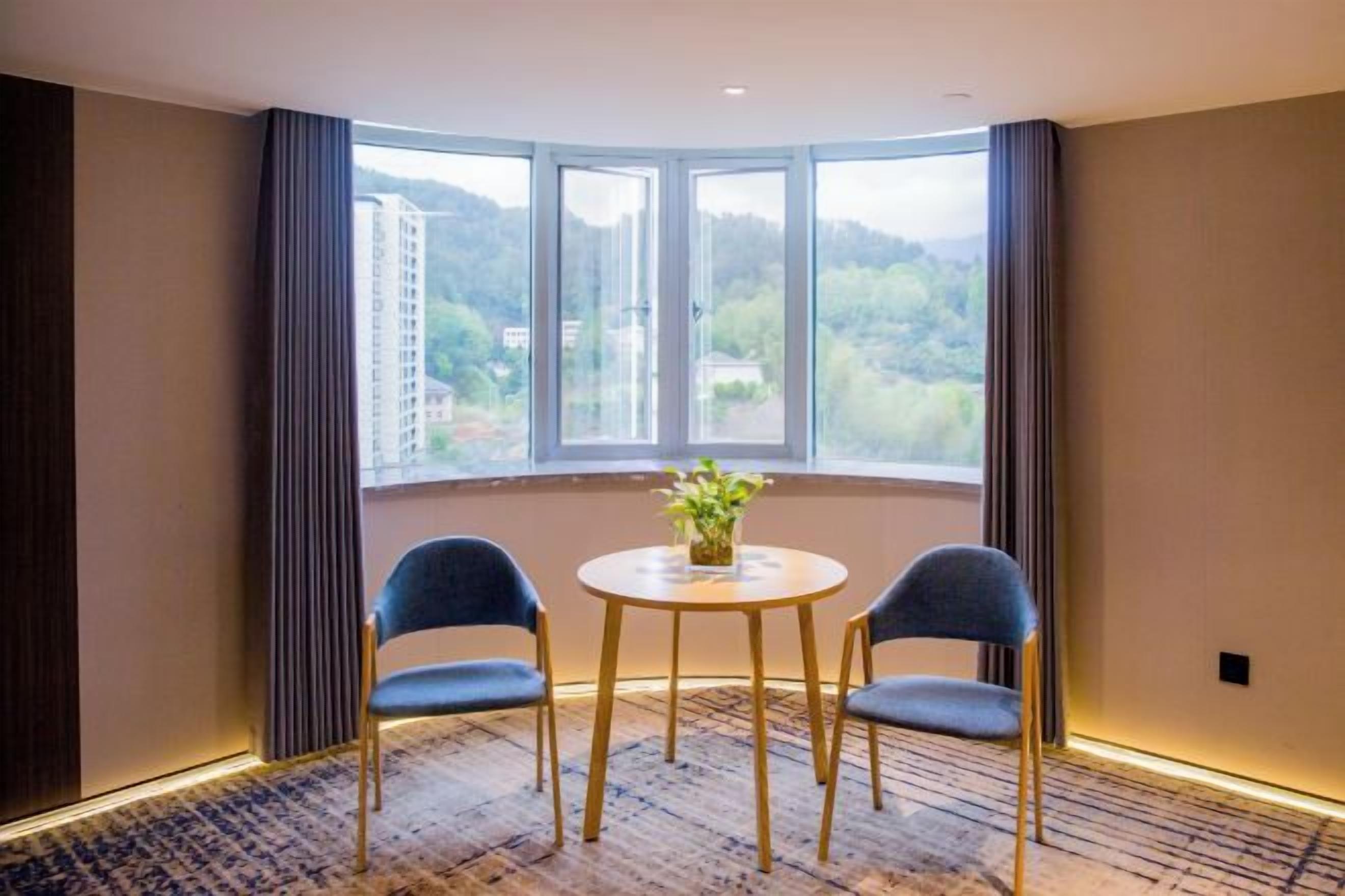 A room with a large window, two chairs, a small table, and a potted plant.