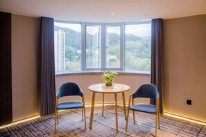 Ein Zimmer mit großem Fenster, zwei Stühlen, einem kleinen Tisch und einem Blumentopf.