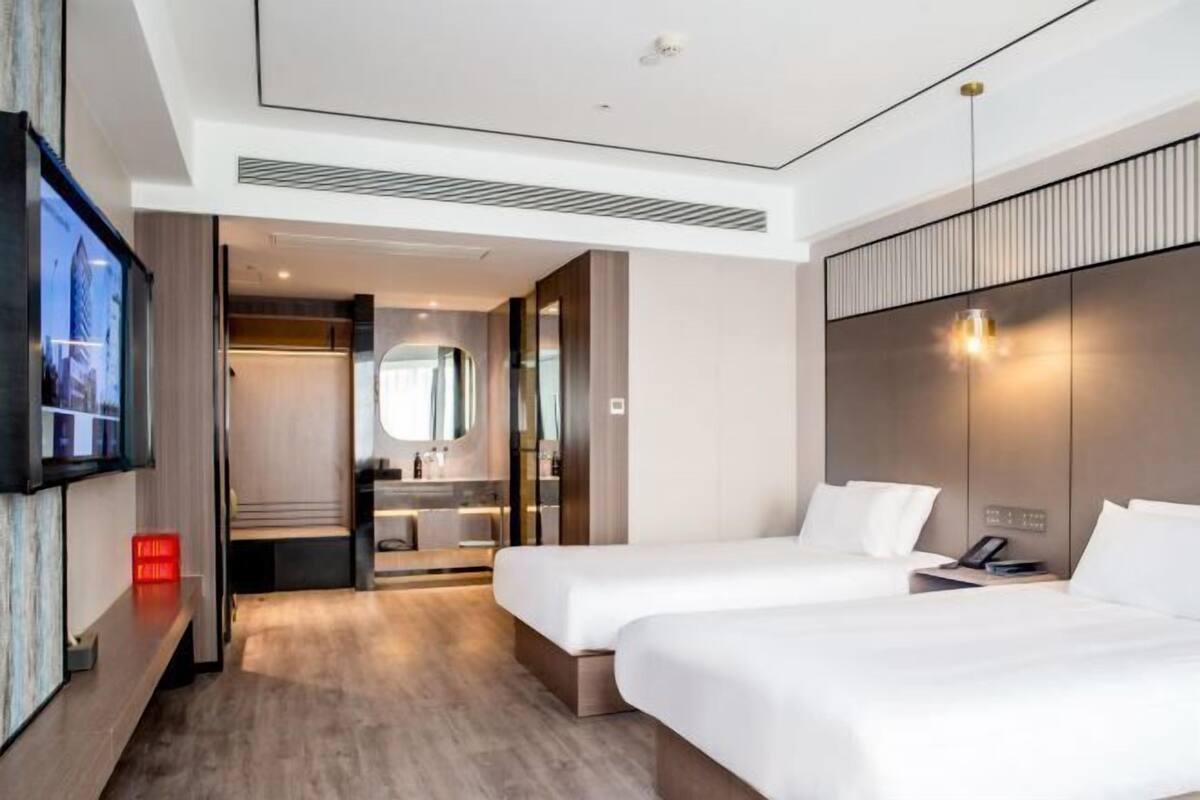 Une chambre d’hôtel avec deux lits, une télévision, un miroir et une salle de bain avec douche et lavabo.