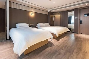 Quarto de hotel moderno com duas camas, piso de madeira e um espelho grande.