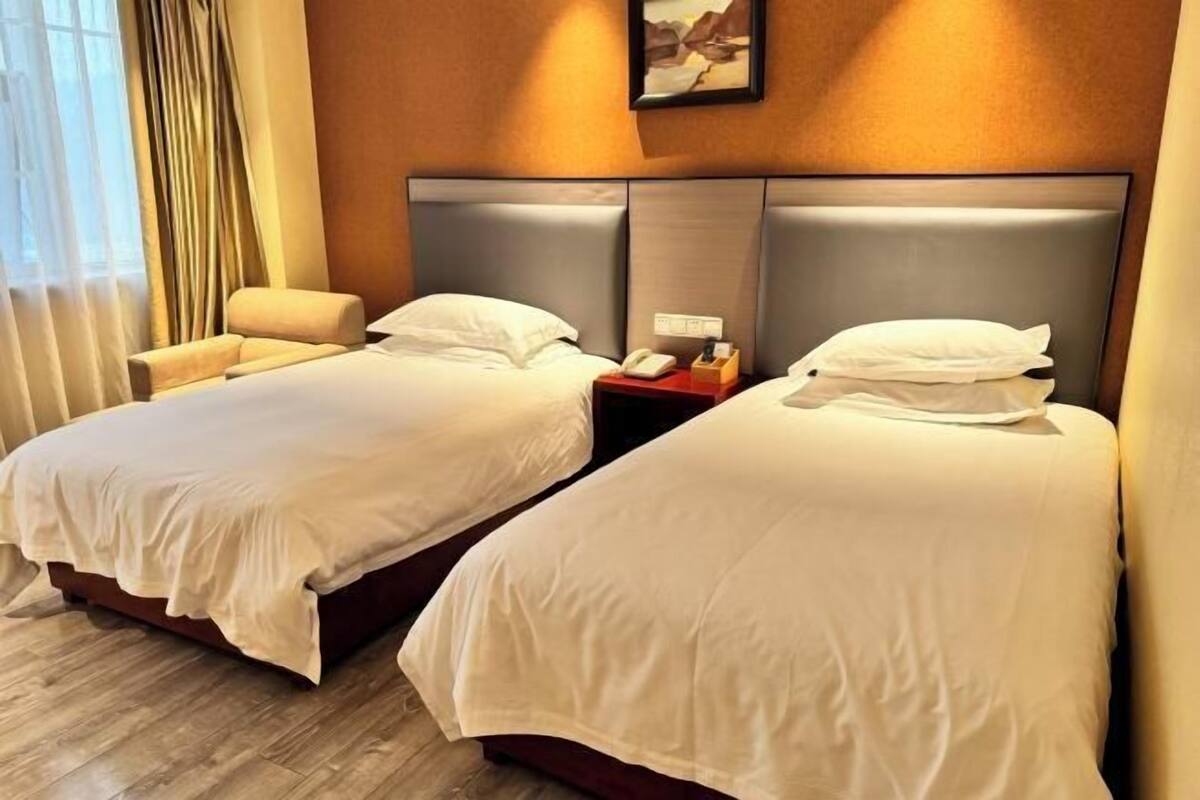Une chambre d’hôtel avec deux lits, une table de chevet, une chaise et une fenêtre avec des rideaux.