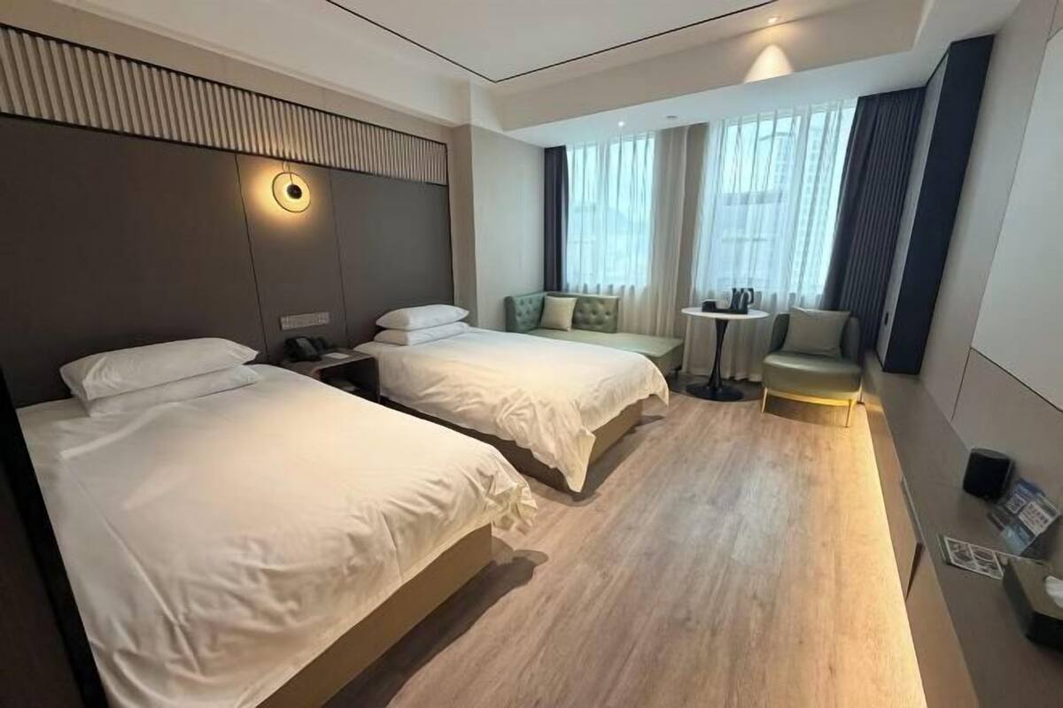 Une chambre d’hôtel avec deux lits, une petite table, une chaise et une fenêtre avec des rideaux.