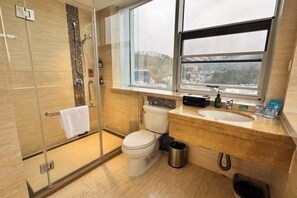 A modern bathroom with a glass-enclosed shower, a toilet, and a sink with a window above. - Kan Hotel (Suichang)
