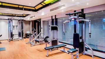 A gym with various exercise equipment, wooden flooring, and large windows.