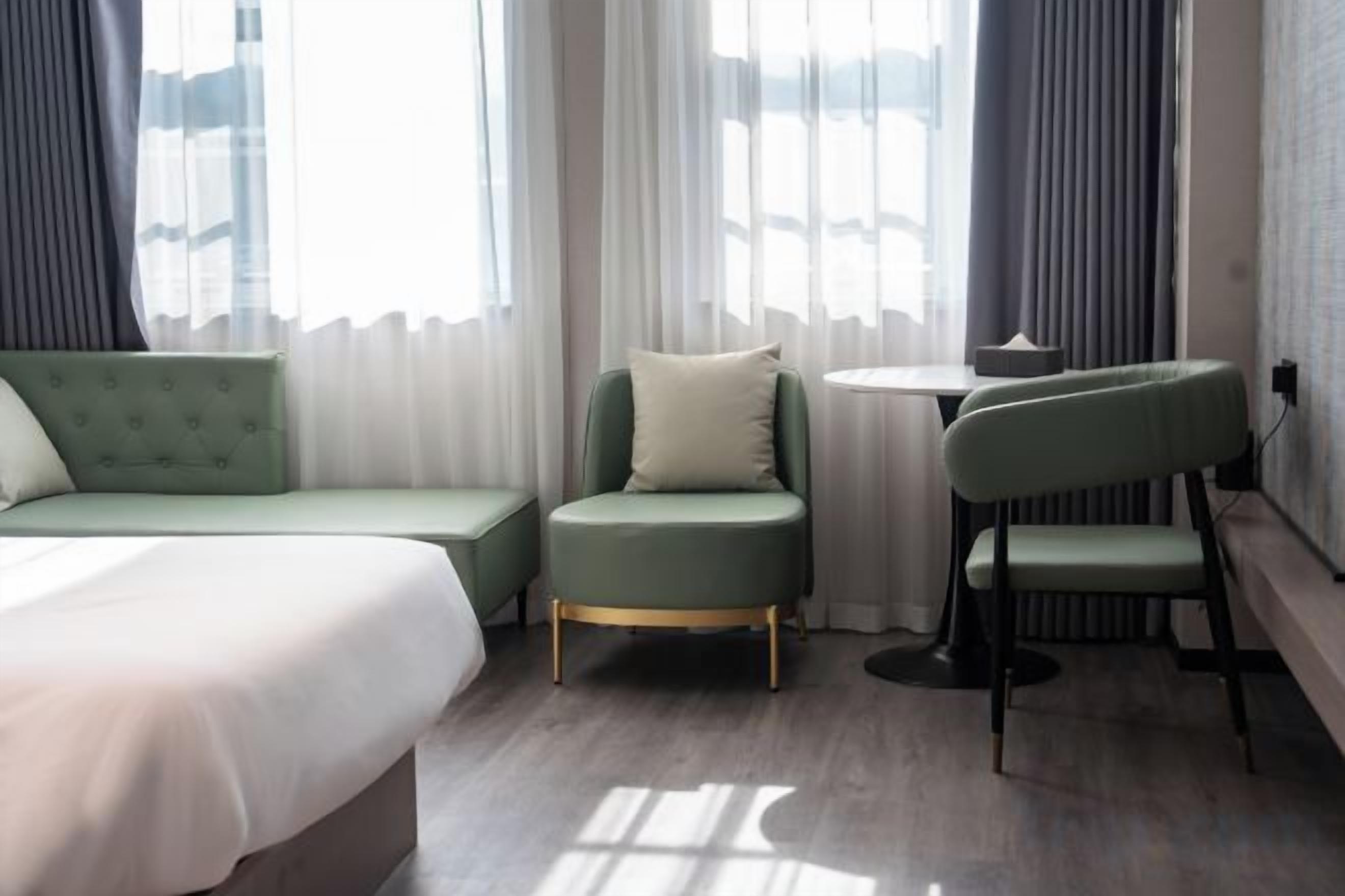 A hotel room with a bed, a green sofa, a small table, and a chair.