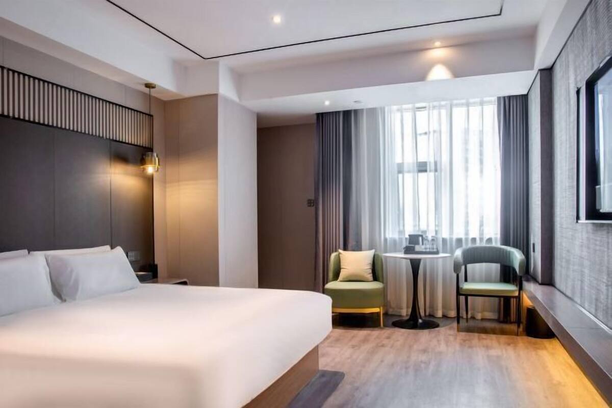 Une chambre d’hôtel moderne avec un grand lit, une petite table, deux chaises, une fenêtre avec des rideaux et un téléviseur fixé au mur.