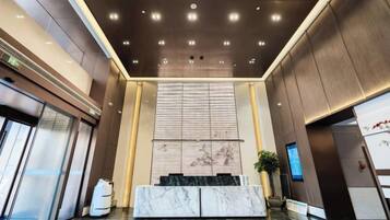 A modern lobby with a marble reception desk, a large wall-mounted screen, and a ceiling with recessed lighting.