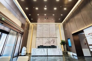 A modern lobby with a marble reception desk, a large wall-mounted screen, and a ceiling with recessed lighting. - Kan Hotel (Suichang)