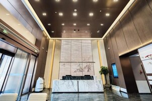Un vestíbulo moderno con una recepción de mármol, una pantalla grande de pared y un techo con iluminación empotrada.