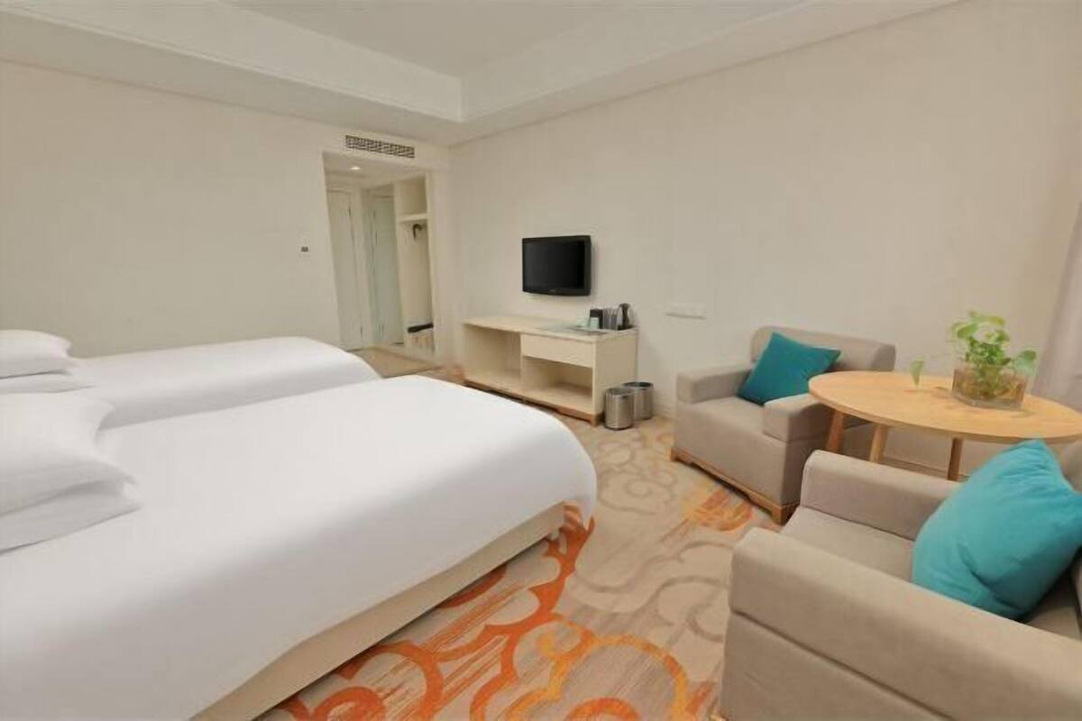 Une chambre d’hôtel avec deux lits, une télévision, un bureau, un canapé et une petite table avec une plante.