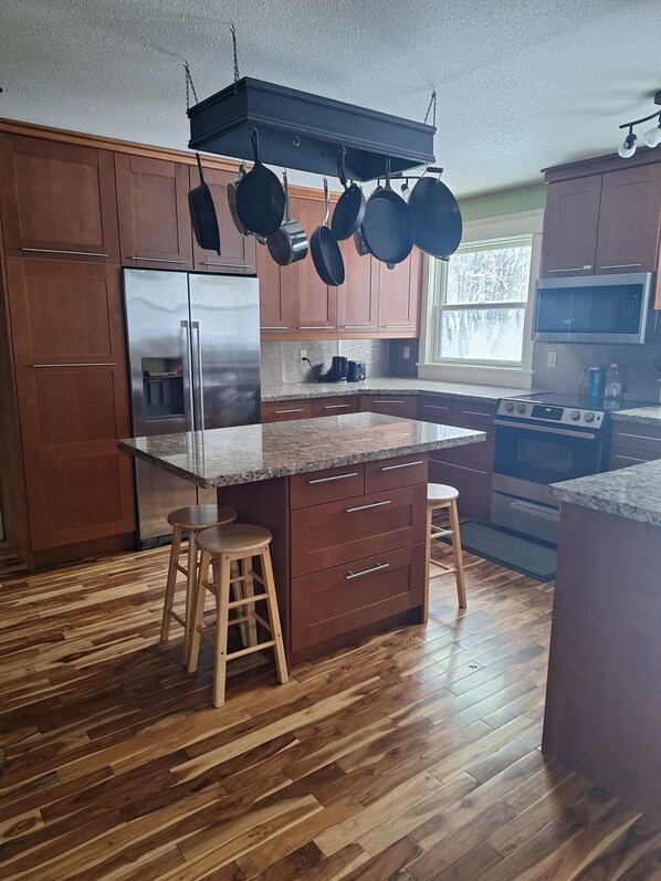 A modern kitchen with wooden cabinets, a stainless steel refrigerator, a built-in oven, and a granite countertop.