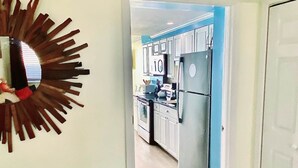 A bedroom with a bed, a decorative mirror, and a view into a kitchen with cabinets and appliances.