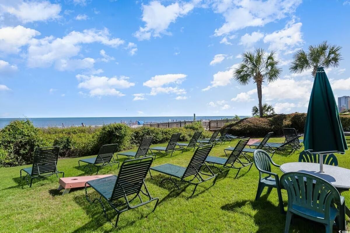 Un espace extérieur aménagé avec des chaises et des tables, offrant une vue sur la plage et bordé de palmiers.