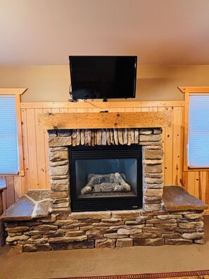 A stone fireplace with a television above it, flanked by wooden walls.