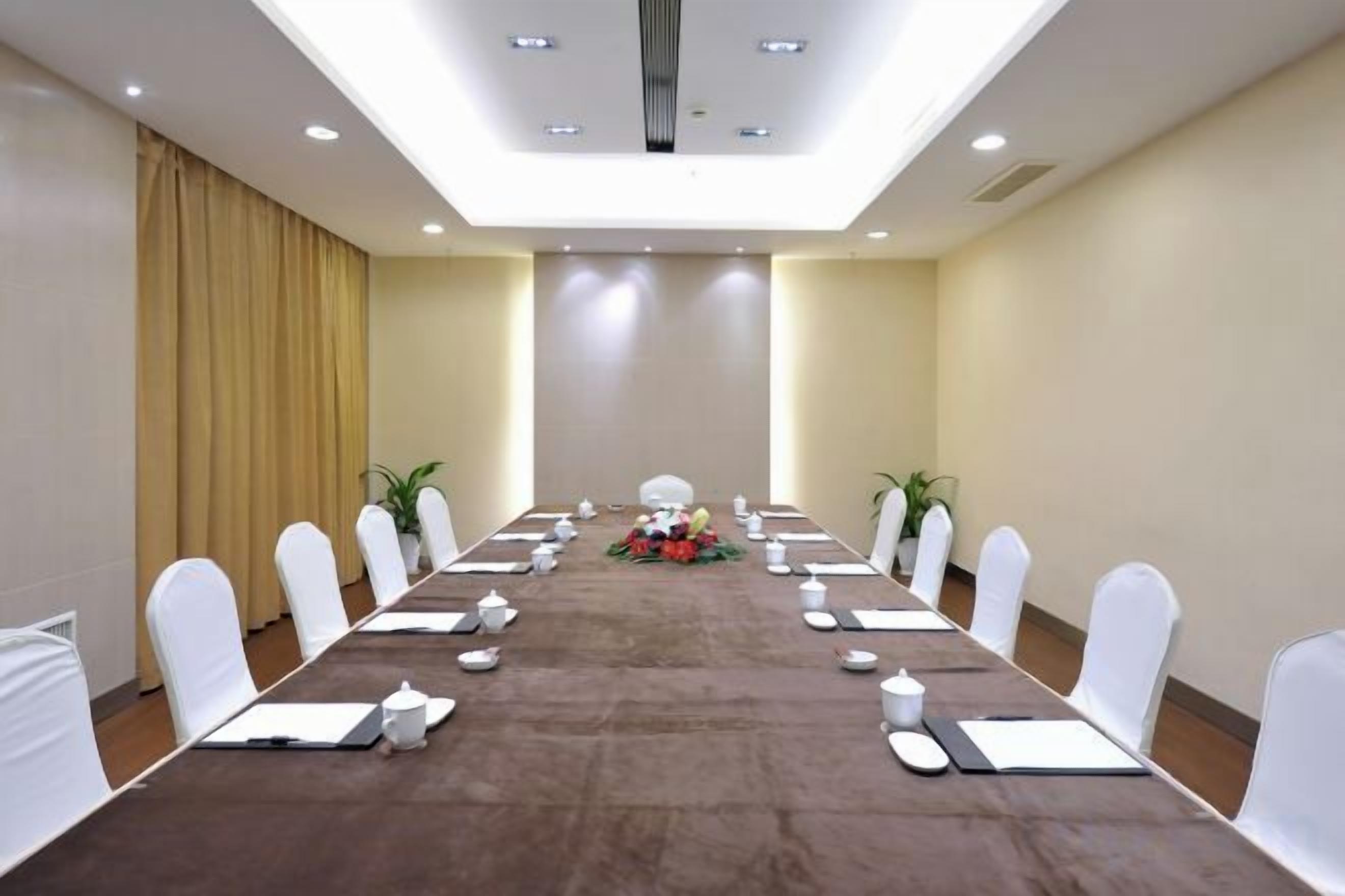 A conference room with a long table, white chairs, and a chandelier.