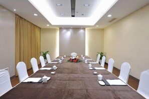 Un salón de conferencias con una larga mesa, sillas blancas y una araña.