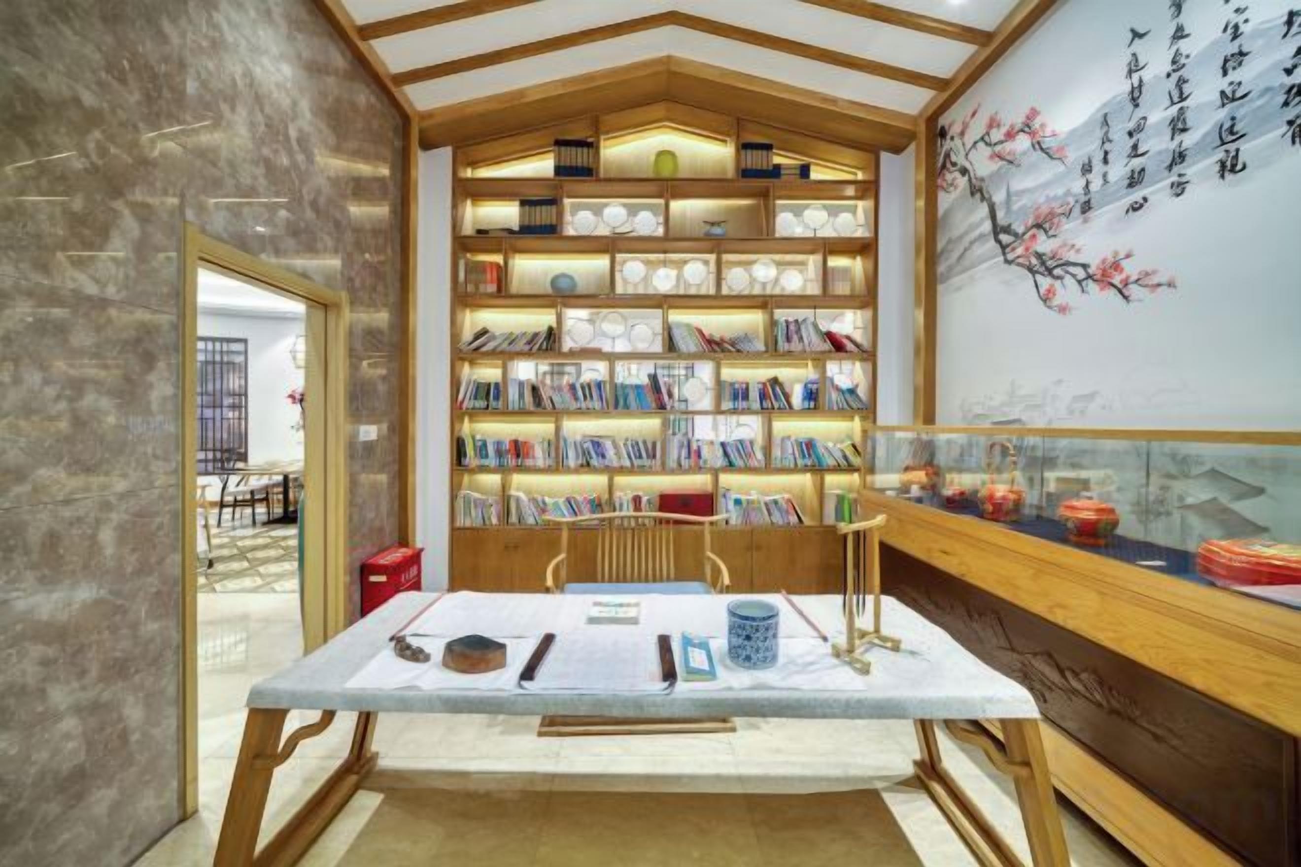 A traditional Chinese tea house with a wooden bookshelf filled with books, a table with tea utensils, and a wall with calligraphy.