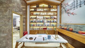A traditional Chinese tea house with a wooden bookshelf filled with books, a table with tea utensils, and a wall with calligraphy.