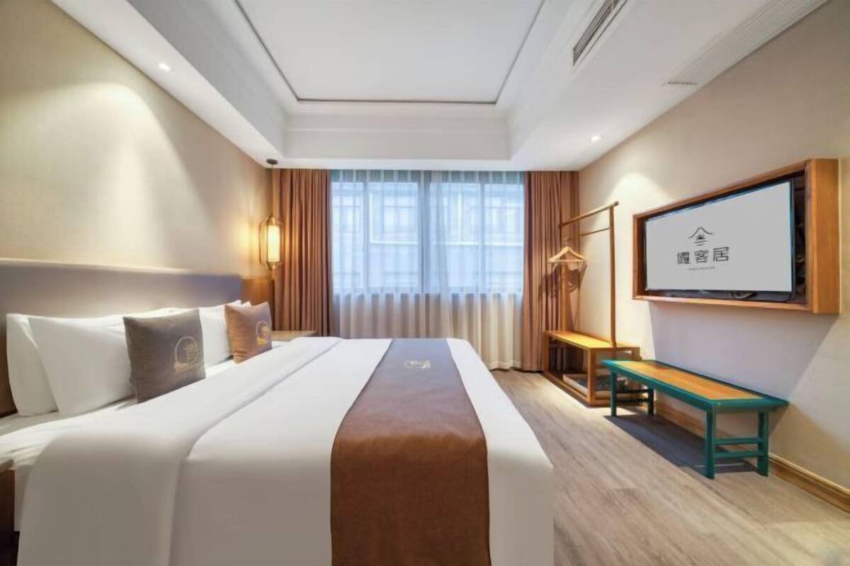 A hotel room with a bed, a desk, a television, and a window with curtains.