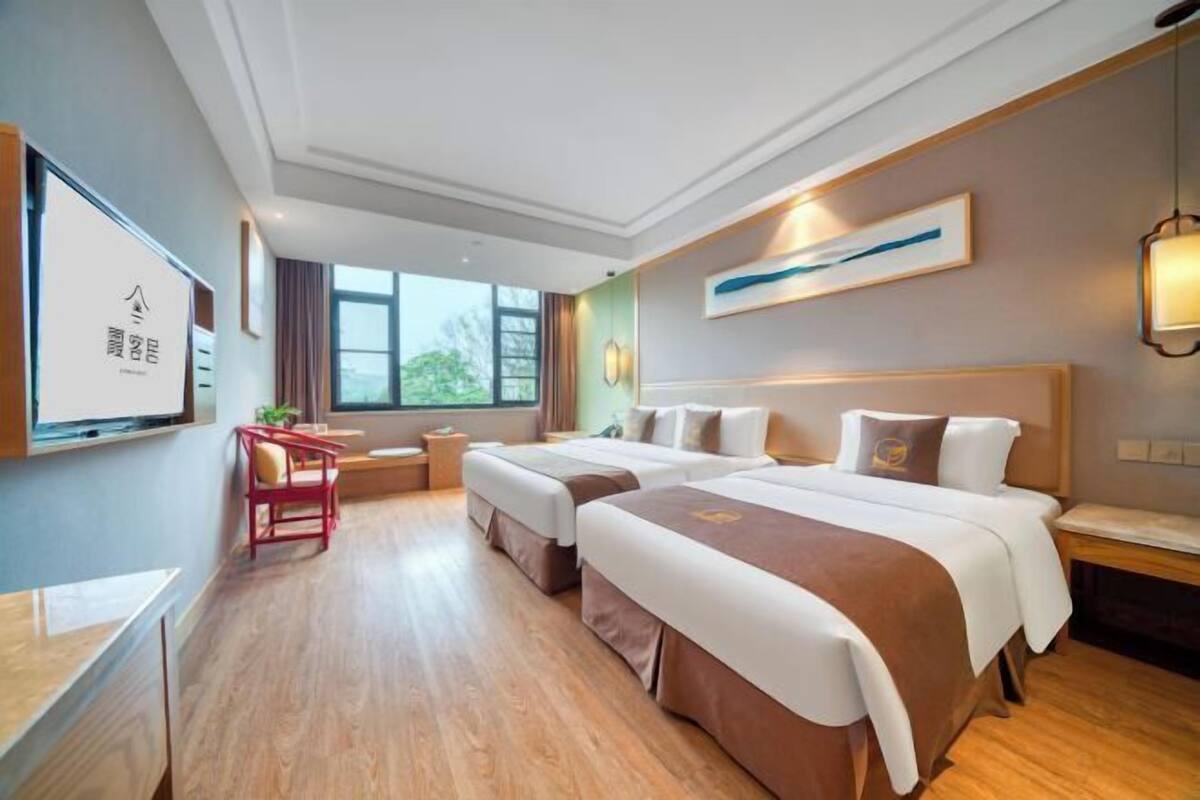 A hotel room with two beds, a desk, a chair, a TV, and a window with a view.