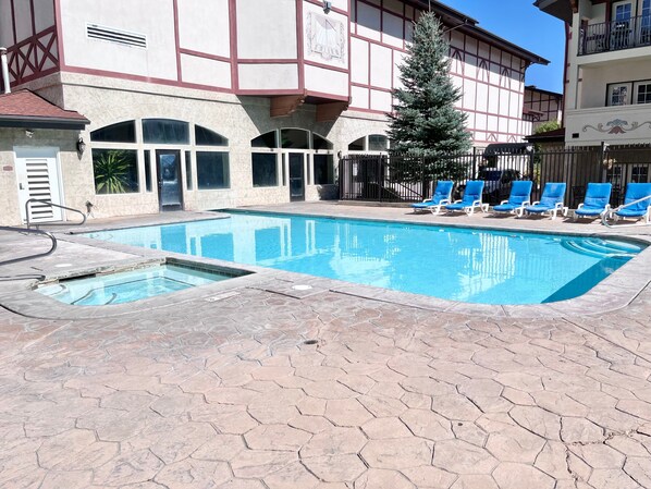 A swimming pool with a tiled deck, a few lounge chairs, and a building with a traditional architectural style in the background.