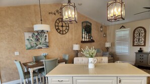 A kitchen with a central island, dining table, chairs, and a sofa. There are pendant lights, wall decor, and a window with blinds. - Heated Pool/cozy/highly recomended/premier host/Elegant/close to many activities (Cape Coral)