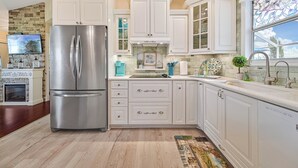 A modern kitchen with white cabinetry, a stainless steel refrigerator, a stone backsplash, and a window with a stained glass view. - Heated Pool/cozy/highly recomended/premier host/Elegant/close to many activities (Cape Coral)