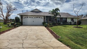 A residential house with a stone driveway, a garage, and a well-maintained lawn. - Heated Pool/cozy/highly recomended/premier host/Elegant/close to many activities (Cape Coral)