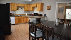 A kitchen with wooden cabinets, a dining table with chairs, and a refrigerator. - Cozy Coastal Getaway (Ingleside)