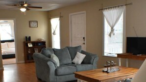A living room with a grey sofa, wooden coffee table, and a ceiling fan. - Cozy Coastal Getaway (Ingleside)