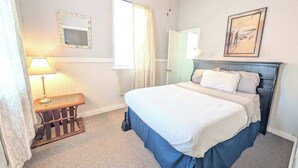 A bedroom with a bed, a bedside table, a lamp, a mirror, a door, and a painting on the wall.