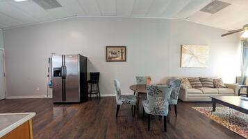 A modern living room with a dining area, a sofa, a coffee table, and a refrigerator.