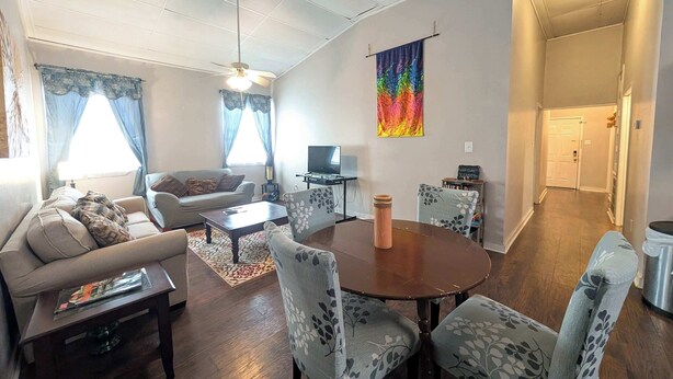 A living room with a sofa, a coffee table, a dining table with chairs, a TV, and a colorful tapestry on the wall. - Chapel Summary:<br>🏡 Wel (Ingleside)