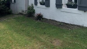 Une maison blanche aux volets gris, un petit jardin et un ciel dégagé.