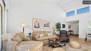 A spacious living room with a large sofa, a coffee table, and a chair. There are two framed pictures on the wall and a potted plant.